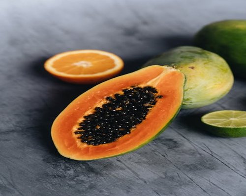 Sliced ripe papaya and whole mangoes on a rustic background